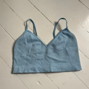 Ljusblå ribbad linnetopp med smala axelband - Säljer en ljusblå ribbad linnetopp med smala axelband och v-ringning från Pieces. Toppen är croppad och har en mjuk, stretchig känsla som passar perfekt till sommaren. Är väldigt stretchigt, därför den ser liten ut på bilden. Passar både S och M. Blir billigare vid köp av flera. Skriv för flera bilder🩵