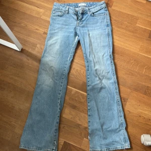 Ljusblå bootcut jeans från Gina tricot  - Säljer ett par ljusblå jeans från Gina tricot  med klassisk femficksdesign och bootcut-ben. Jeansen har normal passform och är tillverkade i denim med dragkedja och knapp framtill. Perfekta för en avslappnad stil. En knapp på fickorna saknas men annars i väldigt bra skick 