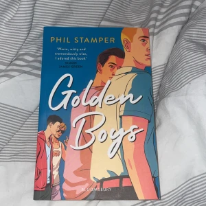 Golden Boys - Säljer boken 'Golden Boys' av Phil Stamper. Omslaget har en färgglad illustration av tre killar i olika kläder mot en blå bakgrund. Boken är på engelska och handlar om vänskap, identitet och att växa upp som queer på en liten ort.