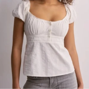 Vit blus med puffärm från Nelly - Säljer en söt vit blus från Nelly med puffärmar och knappar framtill. Blusen har en markerad midja och lätt rynkade detaljer vid bysten. Perfekt till jeans eller kjol för en fräsch look.