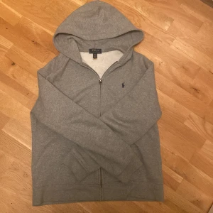 Grå hoodie från Polo Ralph Lauren - Säljer en klassisk grå hoodie från Polo Ralph Lauren med dragkedja och huva. Säljer pga att den är för liten