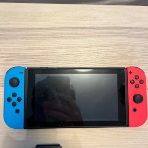 Nintendo Switch med blå och röd Joy-Con - Säljer en Nintendo Switch med blå och röd Joy-Con. Konsolen har en stor skärm och tydliga knappar. Medföljer gör även ett minneskort från SanDisk på 128GB för extra lagring. Perfekt för gaming och portabelt spelande.