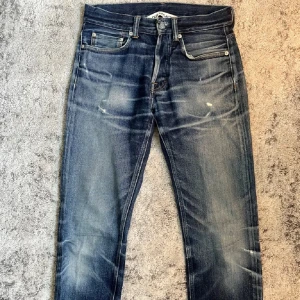 Blå jeansbyxor från Our Legacy - Säljer ett par klassiska blå jeans från Our Legacy med raka ben och knappar i gylfen. Jeansen har en snygg tvätt med slitningar och ljusare partier på låren och knäna. Perfekta för dig som gillar en tidlös denimlook. Helt galna jeans som är ovanliga, samt galen tvätt och detaljer. Ny priset ligger på cirka 4000kr tror jag. Den enda defekten skulle jag säga är där man sätter i knappen på tredje bilden, Man kan fortfarande knäppa och den åker inte ut så man får tolka det hur man vill