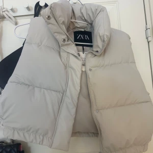 Ljusbeige dunväst från Zara - Säljer en ljusbeige dunväst från Zara med hög krage och dragkedja framtill. Västen är vadderad och har en oversized passform, perfekt för lager-på-lager-stil.Aldrig använd