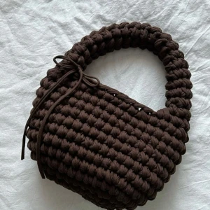 Brun stickad handväska med snörning - Säljer en chunky brun handväska med stickad look och cool snörningsdetalj på sidan. Väskan har ett mjukt, bulligt handtag och är perfekt för dig som gillar unika accessoarer. Rymmer det viktigaste och ger en trendig touch till din outfit.