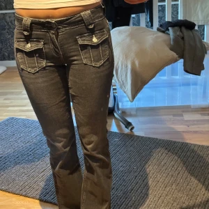 Svarta bootcut jeans från Gina Tricot - Snygga svarta jeans från Gina Tricot med bootcut passform. Jeansen har markerade vita sömmar, stora fickor framtill med lock och knappar samt klassisk dragkedja. Perfekta för dig som gillar en cool och trendig look.