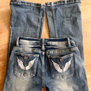 lowwaist bootcut med broderade fickor - Snygga blå jeans med slitningar och coola broderade detaljer, omsydda till lowwaist av en annan tjej. dom har tyvärr vart lite förstora för mig och därför säljer jag dom🌟🍸 skriv om ni vill ha mått