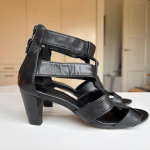 Svarta lädersandaler med klack från Billi Bi, storlek 36 - Snygga svarta sandaler från Billi Bi i skinn med breda remmar och öppen tå. Skorna har en stabil klack och dragkedja bak. Fint skick! Superbekväma!