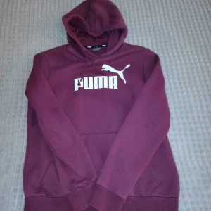 Vinröd hoodie från Puma med logga - Snygg vinröd hoodie från Puma med stor vit logga på bröstet. Tröjan har huva med snörning, magficka och ribbade muddar. Perfekt för chill dagar eller när du vill ha en sportig vibe. Mjuk insida och klassisk passform. Sitter skönt ❤️🌟