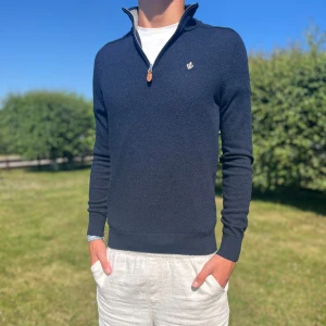 Mörkblå 100% merinoullströja från Morris - Snygg mörkblå stickad tröja från Morris i 100% merinoull. Tröjan har half zip med läderdetalj, liten broderad logga på bröstet och ribbade muddar. Perfekt för lager-på-lager och funkar året runt när du vill vara både chill och stilren.