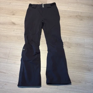 Svarta täckbyxor från Dope XXS - Svarta täckbyxor från Dope i storlek XXS. Byxorna är bootcut, dubbla knappar i midjan och resor i midjan. Perfekta för vintern med slitstarkt material och snygg passform. Snygga detaljer och klassisk look. Perfekta till dig som åker slalom😊