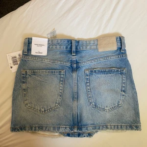 Blå jeanskjol från Pull&Bear S - Snygg ljusblå jeanskjol från Pull&Bear i storlek S. Kjolen har slitna detaljer, fransad nederkant och klassiska fem fickor. Helt ny och aldrig använt