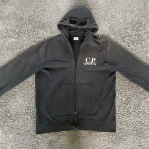 Svart ziphoodie från C.P. Company - Säljer en fet cp company zip hoodie, den är inte använd mycket och är i ett mycket fint skick. Storlek 164 cm men kan även passa större. Den är 100% äkta✅ finns inte kopior på barnstorlekar. Kan skicka bild på qr koden dvs äktighetsbeviset vid förfrågning, frågor? Kontakta mig👌. Allt gott, Noah