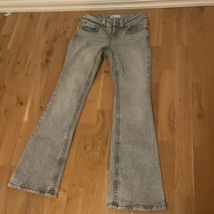 Grå bootcut jeans från Perfect Jeans - Snygga grå bootcut jeans från Perfect Jeans med cool tvättad look. Jeansen har markerade sömmar, stora bakfickor med lock och knapp samt klassisk femficksdesign. Perfekta för dig som gillar en retro vibe och vill sticka ut lite extra.