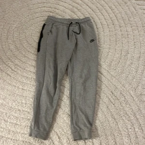 Grå mjukisbyxor från Nike  - Snygga grå mjukisbyxor från Nike i storlek 158-170 Byxorna har resår och snörning i midjan, svarta detaljer och klassisk Nike-logga på benet. Perfekta för chill eller träning, tillverkade i mjukt bomullsmaterial.