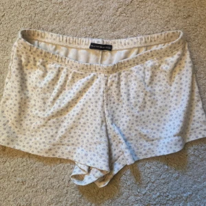 Blommiga shorts från Brandy Melville - Supersöta vita shorts från Brandy Melville med små ljuslila blommor. De är korta, har elastisk midja och är gjorda i mjuk bomull. Perfekta för varma dagar eller som mysplagg hemma. Sitter skönt och har en avslappnad passform. Använda 1 gång 💞