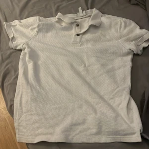 Vit pikétröja H&M slim fit S - Vit pikétröja från H&M i slim fit-modell. Klassisk krage, korta ärmar och knäppning med två knappar framtill. Tillverkad i bomull med lätt struktur i tyget. Perfekt för en clean och fräsch look.