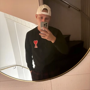 Svart sweatshirt från Ami Paris med hjärtdetalj - Svart sweatshirt från Ami Paris med rund halsringning och en röd hjärtdetalj med bokstaven A broderad på bröstet. Tröjan har långa ärmar, ribbade muddar och är tillverkad i mjuk bomull. Perfekt för en stilren och trendig look. Inga lappar tyvärr 