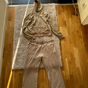 Beiga mjukisbyxor Juicy Couture XL - Supermjuka beiga mjukisbyxor från Juicy Couture i velour med bred resår och snörning i midjan. Byxorna har lite utsvängda ben och stora fickor framtill. Perfekta för chill eller när du vill ha en avslappnad look.