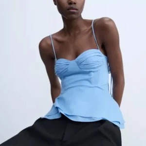 Ljusblå linnetopp med tunna axelband - Supersöt ljusblå linnetopp med tunna axelband och snygg rynkad detalj vid bysten. Toppen har en lätt utsvängd nederdel som ger en somrig känsla. Perfekt för varma dagar och enkel att styla med både jeans och kjol.