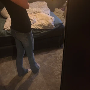 Blå bootcut jeans med slitna detaljer - Säljer ett par blå bootcut jeans med låg midja och slitna detaljer vid knä och benslut. Jeansen har klassisk femficksdesign och är gjorda i jeansmaterial. Perfekta för dig som gillar en avslappnad och trendig look. Ena skärp hålet är söndrigt derföe nedsatt pris 