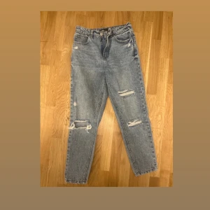  ljusblå ripped jeans - Säljer ett par klassiska jeans i ljusblå tvätt med snygga slitningar och hål på knäna. Jeansen har rak passform, fem fickor och hög midja. Perfekta för en avslappnad och trendig look.