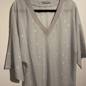 Oversized blus från Capital B - Oversized grå t-shirt från Capital B med vita prickar och bred v-ringning. T-shirten har korta ärmar och är tillverkad i ett mjukt, lätt material som känns skönt mot huden. Perfekt för dig som gillar en chill och avslappnad stil. Luftigt plagg! Är helt ny, men pris-taggen har fallit bort! , säg till för fler bilder! 