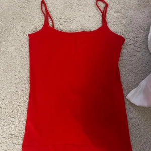 Röd linnetopp med smala axelband - En enkel och snygg röd linnetopp med smala axelband. Perfekt för varma dagar eller att styla lager på lager. Tidlös modell som är lätt att matcha med jeans eller kjol.