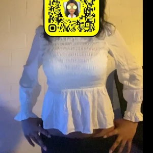 Vit blus med smock och volang - Supersöt vit blus med smockad överdel och volang nertill. Långa ärmar med smock vid handlederna ger en romantisk vibe. Perfekt att styla med jeans eller kjol för en trendig look.