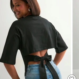 Svart bolerotopp med knyt i ryggen - Trendig svart bolerotopp med öppen rygg och breda knytband som ger en snygg detalj. Toppen har halvlånga ärmar och croppad passform, perfekt att styla med höga jeans för en cool look.