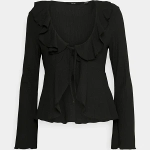 Svart blus med volang och knyt från vero Moda - Supersnygg svart blus från vero Moda med långa ärmar, volangdetaljer längs urringningen och ett sött knyt framtill. Materialet är löst och bekvämt den är i storlek S. och aldrig använt.