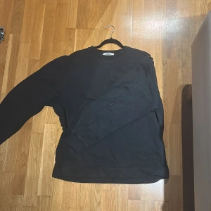 Svart sweatshirt från Stone Island L - Svart sweatshirt från Stone Island i storlek L. Tröjan har rund hals, långa ärmar och diskret broderad logga på bröstet. Tillverkad i mjuk bomull som är skön att bära. Perfekt för en clean och stilren look. Ny pris 4000 köpt i butik, nk i Stockholm.