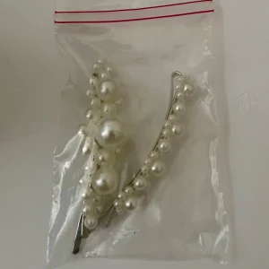 *NY*Pärlprydda hårnålar i silver - Nya oanvända. Två snygga hårnålar med vita pärlor på silvrig metallbas. Perfekt accessoar för att ge frisyren en extra touch av elegans. Passar till både utsläppt och uppsatt hår.