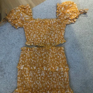 Fint det från Princess Polly - Superfin gul  topp med vita blommor och volangdetaljer. Toppen har korta puffärmar med knyt och smockad passform som sitter tajt. Fin kjol som matchar till. De är helt nya och nypris ligger runt 700kr💓