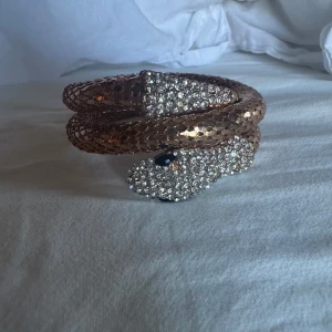Glittrigt orm-armband i guld - Säljer ett unikt armband format som en orm i guld med glittrande stenar på huvudet och svansen. Armbandet är flexibelt och snurras runt handleden för en cool och iögonfallande look.