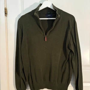 Olivgrön tröja med dragkedja från Boomerang - Säljer en olivgrön tröja från Boomerang i ekologisk bomull. Tröjan har hög krage och dragkedja framtill, samt ribbade muddar vid ärmslut och nederkant. Perfekt för lager-på-lager och snygg till jeans.