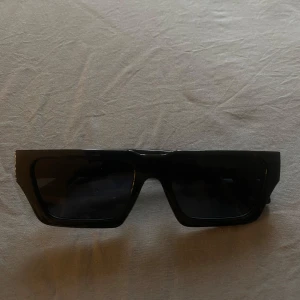 Solglasögon - Snygga svarta solglasögon från Easy med rektangulära, breda bågar och mörka glas. Glasögonen har en modern och kantig design som ger en cool look. Perfekta för dig som vill sticka ut med en trendig accessoar. Köpte för 350 kr