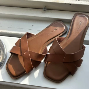 Bruna sandaler med korsade remmar - Snygga bruna sandaler från H&M med breda korsade remmar och fyrkantig tå. Perfekta för varma dagar och enkla att matcha till olika outfits. Gjorda i syntetmaterial med platt sula för en bekväm känsla. Perfekta tofflorna inför sommaren!!☀️☀️