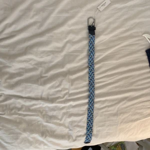 Flätat bälte från Onewear - Säljer ett snyggt flätat bälte från Onewear i olika blå nyanser med inslag av beige. Bältet har silverfärgat spänne och detaljer i mörkblått skinn. Perfekt accessoar för att lyfta din outfit. Helt nytt, aldrig använt därför att jag köpte en för liten storlek, har till och med lappen kvar.