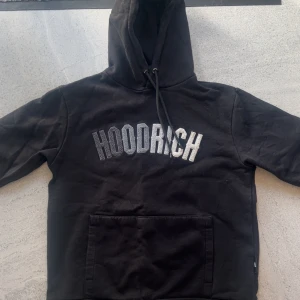 Svart hoodie från Hoodrich - Säljer en svart hoodie från Hoodrich i storlek M. Tröjan har en stor magficka framtill, huva med dragsko och HOODRICH-logga broderad i vitt och grått på bröstet. Perfekt att matcha till.