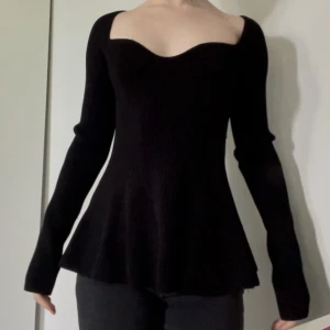 Svart ribbad topp med sweetheart-urringning - Säljer en svart långärmad topp med ribbad struktur och snygg sweetheart-urringning. Modellen är figurnära upptill och har utsvängd nederdel som ger en fin siluett. Perfekt för dig som vill ha en stilren men ändå unik topp. Storlek S men jag på bild är XS och uppskattar att den passar storlek M bättre därför att den är stor i storlek.