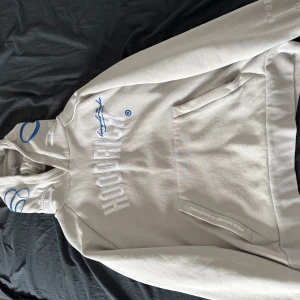 Hoodrich hoodie - Säljer en beige hoodie från Hoodrich med vit broderad logga och blå detaljer. Hoodien har magficka, huva och tryck både fram och bak. Perfekt för en avslappnad streetwear-look.
