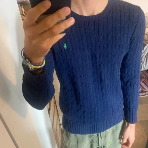 Ralph Lauren tröja - Klassisk kabelstickad tröja från Ralph Lauren. Snygg ljusare marinblåfärg med grön logga. Storlek 18-20 år. Passar S/M