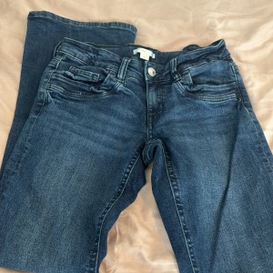 Mörkblå bootcut jeans från Gina Tricot - Säljer ett par mörkblå jeans från Gina Tricot med bootcut-modell. Jeansen har klassiska fem fickor, knapp och dragkedja framtill samt snygga slitningar för en cool look.