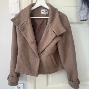 Kappa - Jättefin och stilren kort kappa från NAKD! Använd men i bra skick! Jättefin beige färg och passar till i princip allt! Originalpris ca 500kr