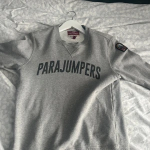 Grå sweatshirt från Parajumpers - Säljer en grå sweatshirt från Parajumpers med stor logga på bröstet och patch på ärmen. Tröjan har rund halsringning och långa ärmar. Mjuk insida i fleece och klassisk passform. Perfekt för en avslappnad stil. Storlek smal!