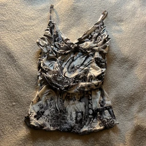 Svartvit y2k topp - Säljer en unik svartvit linnetopp med konstnärligt mönster och smala axelband. Toppen har en lätt rynkad detalj framtill.