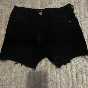 Svarta jeansshorts från LAB Industries - Svarta jeansshorts från LAB Industries med råa kanter och klassisk femficksdesign. Knappar och dragkedja framtill. Perfekta för varma dagar och enkel att matcha med olika toppar.