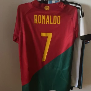 Portugal fotbollströja Ronaldo 7 - Säljer en Portugal landslagströja med Ronaldo och nummer 7 på ryggen. Tröjan är röd och grön med gula detaljer och har landslagets emblem på bröstet. Klassisk kortärmad modell från Nike, perfekt för fotbollsfans.