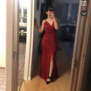 Röd långklänning med slits - Säljer en elegant röd långklänning med figurnära passform och snygg slits framtill. Perfekt för bal eller fest. Klänningen har en enkel och stilren design utan ärmar och är tillverkad i ett mjukt, följsamt material.